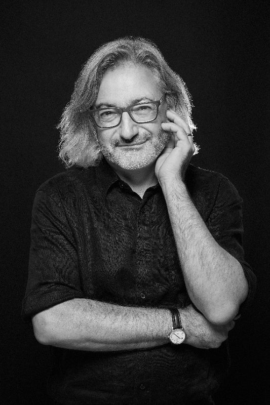Black and white portrait of a man with glasses and a watch, posing with one hand on his chin.