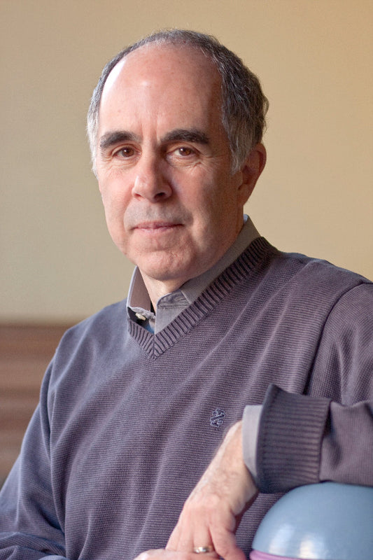 Man wearing a gray sweater with a logo, sitting against a beige wall.