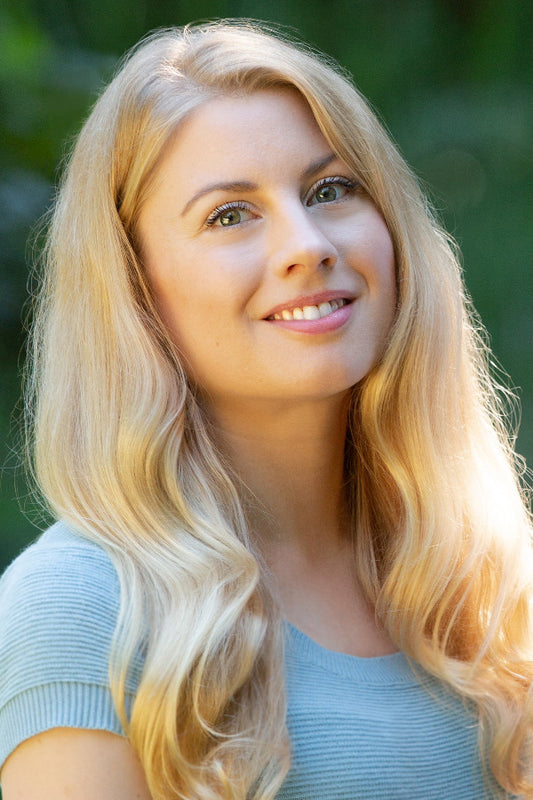 Woman with long blonde hair wearing a light blue top against a blurred green background